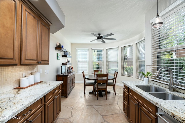 kitchen featuring light stone counters, a sink, baseboards, stainless steel dishwasher, and decorative backsplash