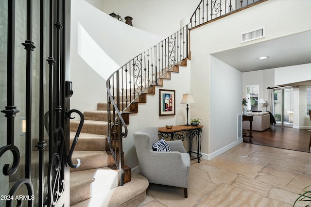 stairway with stone tile flooring, a towering ceiling, visible vents, and baseboards