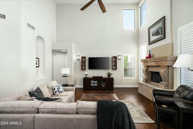 living area featuring dark wood-style flooring, a fireplace with raised hearth, visible vents, a ceiling fan, and baseboards