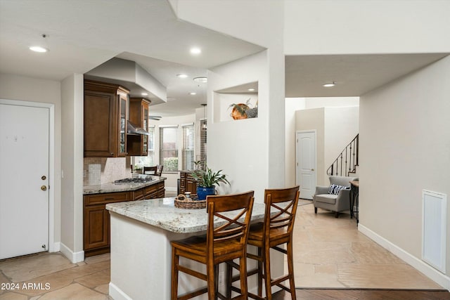 kitchen featuring baseboards, light stone counters, a breakfast bar, stainless steel gas stovetop, and backsplash