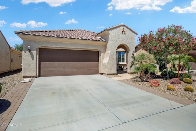 mediterranean / spanish house with an attached garage, stucco siding, a tiled roof, and concrete driveway