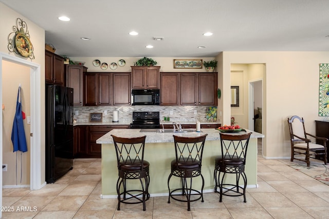 kitchen with decorative backsplash, an island with sink, a breakfast bar area, and black appliances