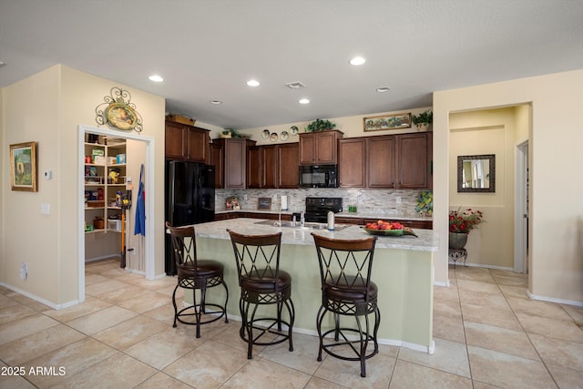 kitchen featuring a breakfast bar, an island with sink, light tile patterned floors, tasteful backsplash, and black appliances