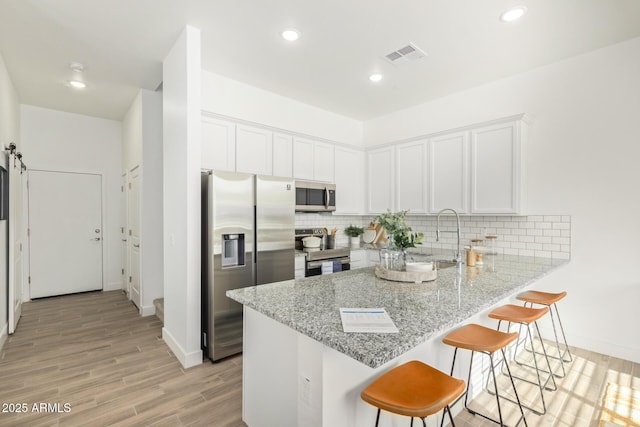 kitchen with appliances with stainless steel finishes, a peninsula, light wood-style floors, baseboards, and recessed lighting