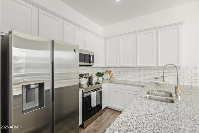kitchen featuring appliances with stainless steel finishes, a sink, white cabinetry, tasteful backsplash, and light stone countertops