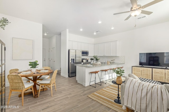 kitchen with stainless steel appliances, a peninsula, decorative backsplash, white cabinets, and light wood-style flooring