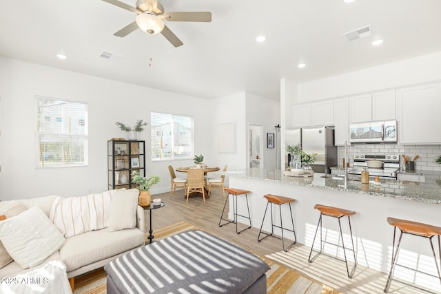 living room featuring light wood-style floors, a ceiling fan, recessed lighting, and baseboards