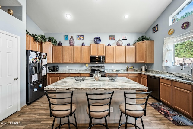 kitchen with a kitchen island, black appliances, a kitchen bar, sink, and light stone counters