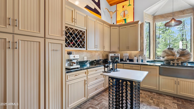 kitchen featuring dark countertops, decorative light fixtures, cream cabinetry, and tasteful backsplash