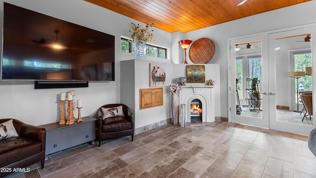 living area featuring a glass covered fireplace, french doors, wooden ceiling, and a ceiling fan