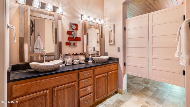 bathroom with double vanity, stone finish flooring, wood ceiling, and a sink