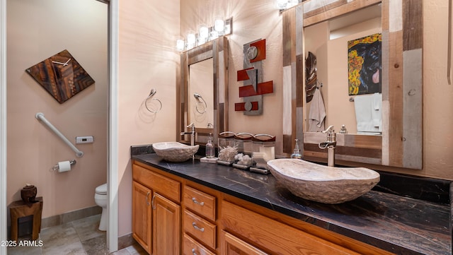 bathroom featuring double vanity, toilet, baseboards, and a sink