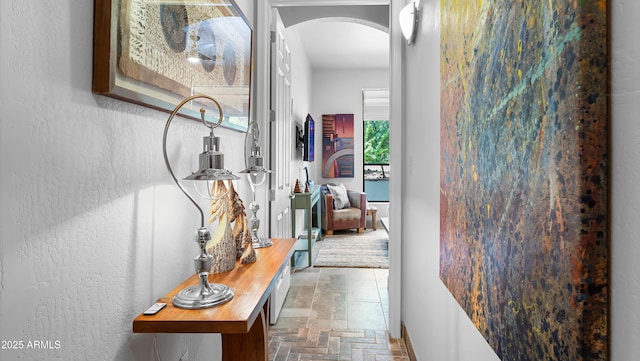 corridor with arched walkways, stone tile floors, and baseboards