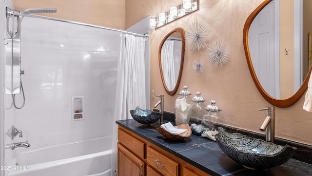 bathroom featuring double vanity, shower / tub combo, a textured wall, and a sink