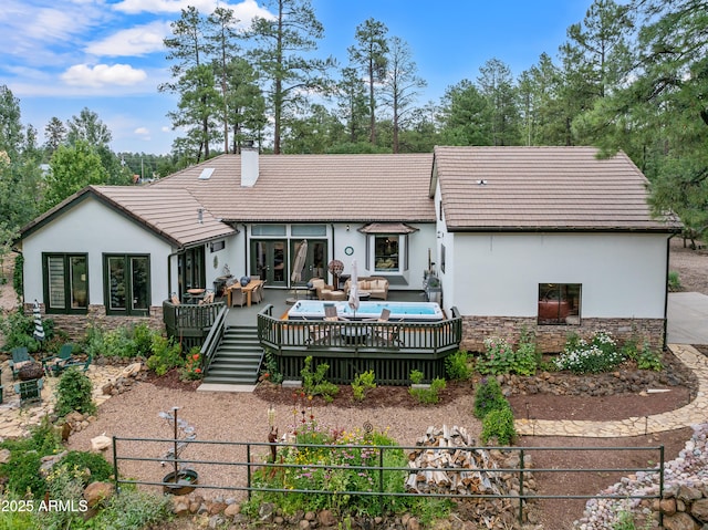 rear view of house featuring a tile roof, stone siding, stucco siding, and a deck