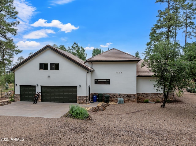 view of home's exterior featuring a tile roof, concrete driveway, stone siding, cooling unit, and stucco siding