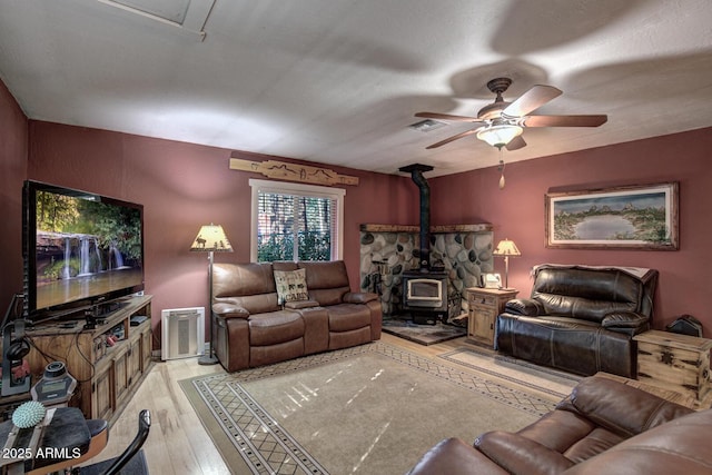 living room with light wood-type flooring, a wood stove, and ceiling fan