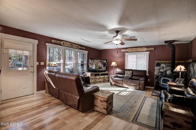 living room with light wood-type flooring, a wood stove, ceiling fan, and a textured ceiling