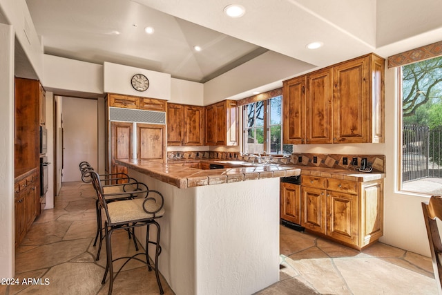 kitchen featuring tile counters, paneled refrigerator, a breakfast bar, and light tile floors