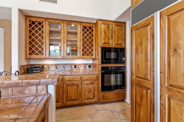 kitchen featuring tile countertops, black appliances, and light tile floors