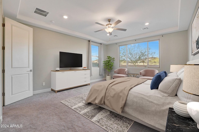 bedroom with ceiling fan, light carpet, and a tray ceiling