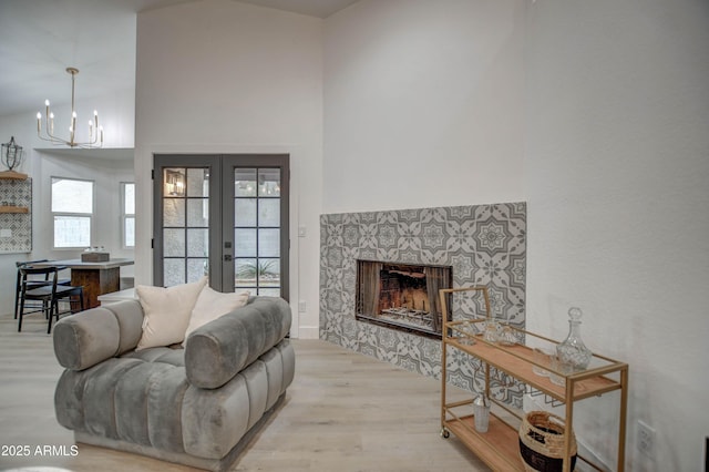 living room with an inviting chandelier, light wood-type flooring, a towering ceiling, a fireplace, and french doors