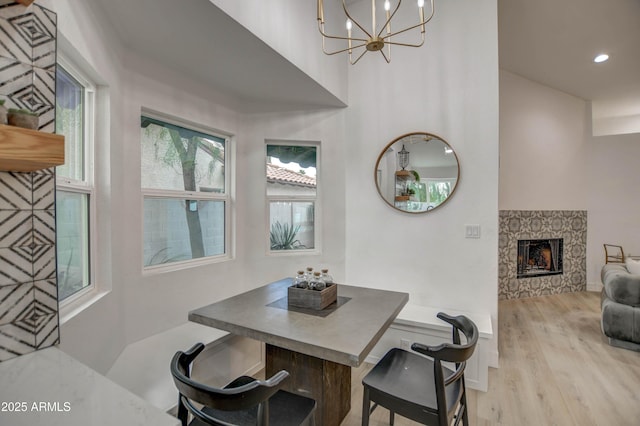 dining area with light wood-type flooring, an inviting chandelier, and a stone fireplace