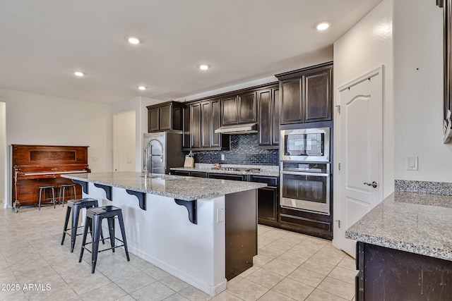 19946 W Glenrosa Ave, Litchfield Park, AZ 85340 - kitchen with a kitchen island with sink, a breakfast bar area, under cabinet range hood, appliances with stainless steel finishes, and backsplash