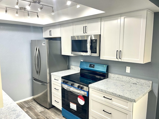 kitchen with white cabinets, appliances with stainless steel finishes, track lighting, and light stone countertops