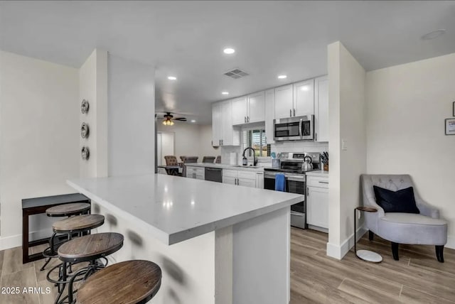 kitchen featuring a kitchen bar, white cabinets, appliances with stainless steel finishes, and kitchen peninsula