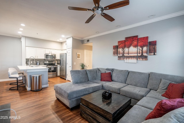 living room featuring a ceiling fan, visible vents, light wood finished floors, ornamental molding, and recessed lighting