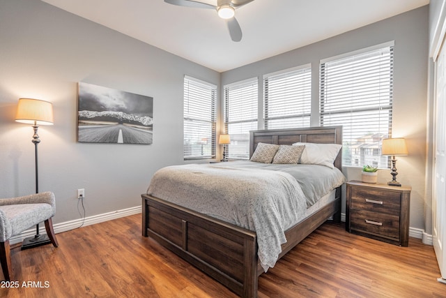 bedroom featuring ceiling fan, baseboards, multiple windows, and wood finished floors