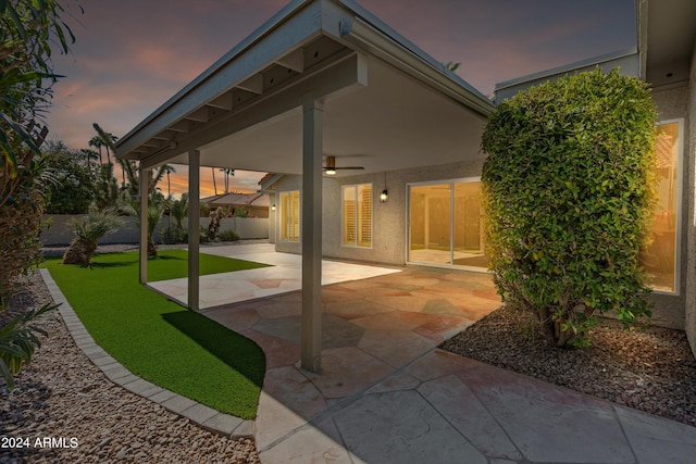 patio terrace at dusk featuring a yard and ceiling fan