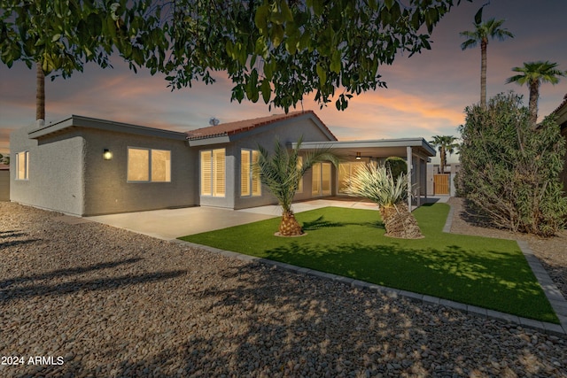 back house at dusk with a lawn and a patio area