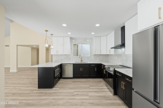 kitchen with hanging light fixtures, kitchen peninsula, wall chimney range hood, appliances with stainless steel finishes, and light hardwood / wood-style floors