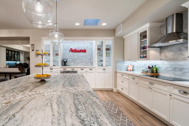 kitchen featuring black electric cooktop, wall chimney range hood, white cabinets, and light hardwood / wood-style floors