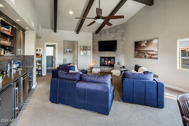 living room with a large fireplace, ceiling fan, beam ceiling, and light carpet