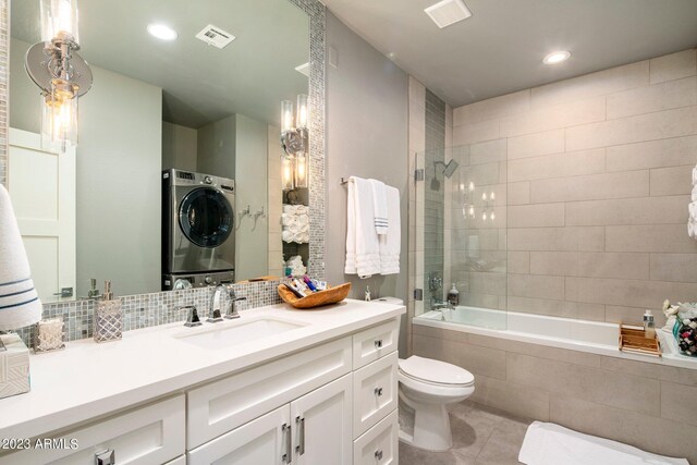 full bathroom with toilet, stacked washer and dryer, tile patterned flooring, vanity, and tasteful backsplash