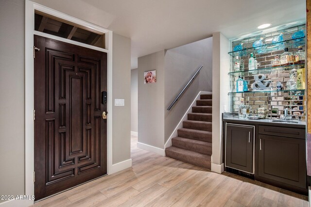 foyer entrance with bar area and light hardwood / wood-style floors