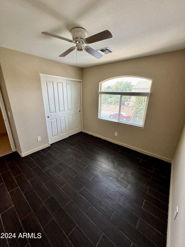 unfurnished bedroom with a textured ceiling, dark wood-type flooring, a closet, and ceiling fan