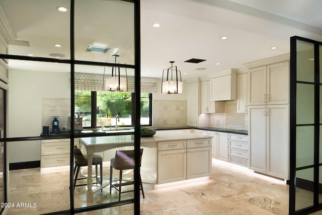 kitchen with tasteful backsplash, hanging light fixtures, sink, cream cabinetry, and a center island