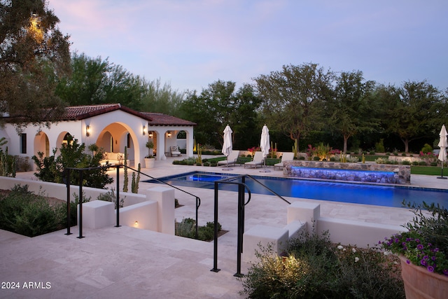 pool at dusk with a patio and pool water feature