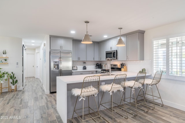 kitchen with stainless steel appliances, a peninsula, light countertops, and gray cabinetry