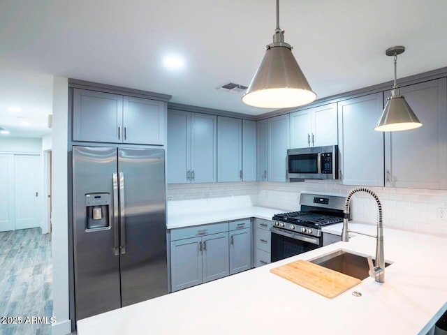 kitchen with a sink, light countertops, appliances with stainless steel finishes, tasteful backsplash, and decorative light fixtures