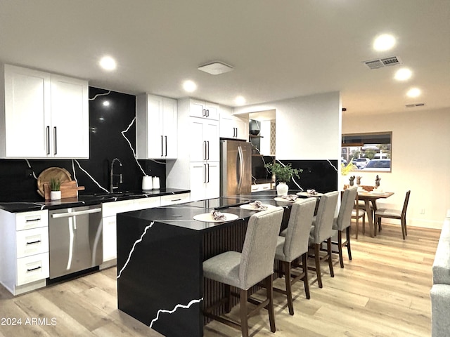 kitchen featuring tasteful backsplash, sink, white cabinets, light hardwood / wood-style floors, and stainless steel appliances