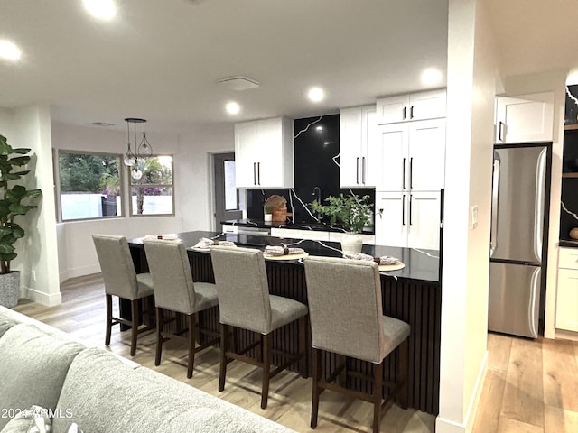 kitchen with a breakfast bar, white cabinetry, decorative light fixtures, light hardwood / wood-style flooring, and stainless steel fridge