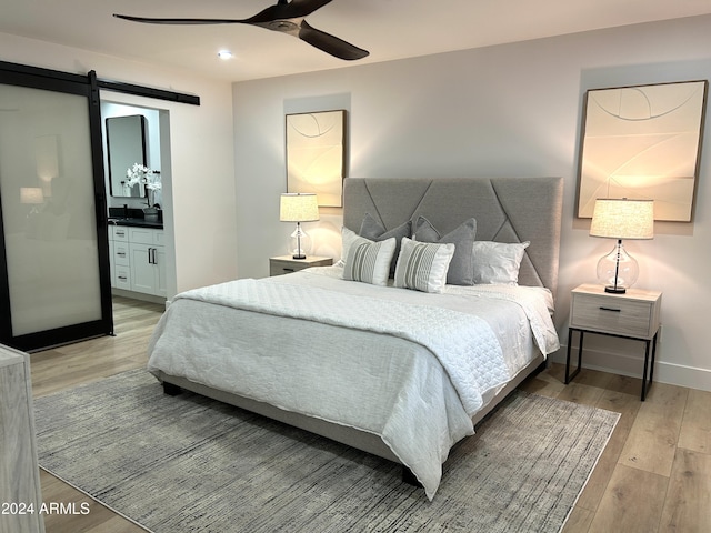 bedroom featuring a barn door, connected bathroom, ceiling fan, and light hardwood / wood-style flooring