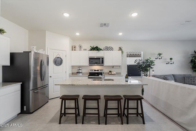 kitchen featuring light stone counters, white cabinets, a center island with sink, and appliances with stainless steel finishes