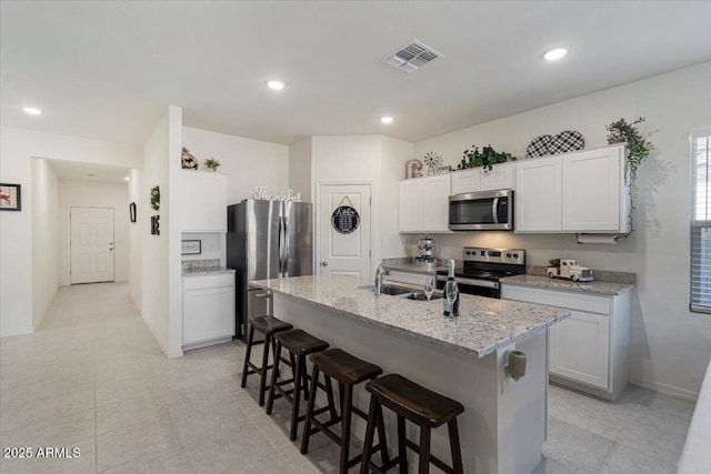 kitchen featuring stainless steel appliances, a center island with sink, white cabinetry, a kitchen breakfast bar, and sink