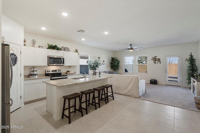 kitchen featuring stainless steel appliances, a center island with sink, light colored carpet, white cabinets, and sink